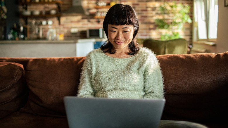 Woman looking at her computer on a couch while smiling
