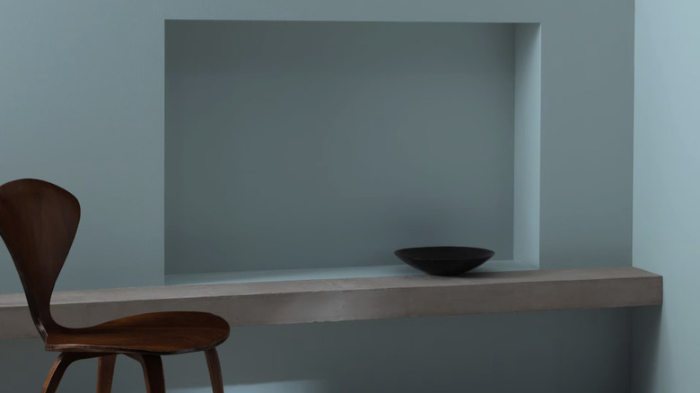 A niche painted a mid-toned gray-blue color styled with a bowl and a wood chair
