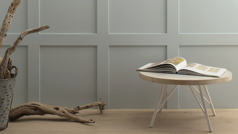 A gray green paint color on a wall behind a small stool and a basket of driftwood