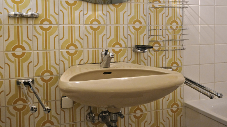 A yellow off-white sink with chrome faucet with a geometric orange, yellow, and off-white tile backsplash.