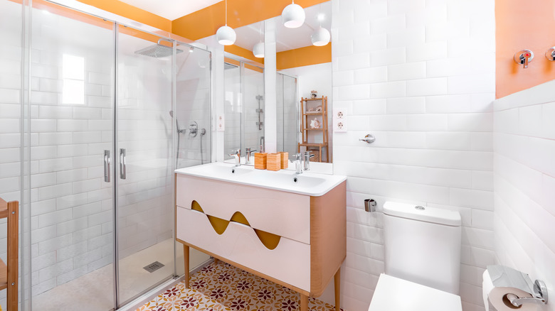 A modern bathroom with orange, white, and brown tiling and a retro wood sink by the toilet.