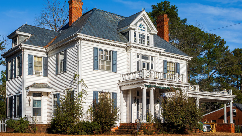 A Victorian style farmhouse painted white with trees on the lawn and blue sky in the background.