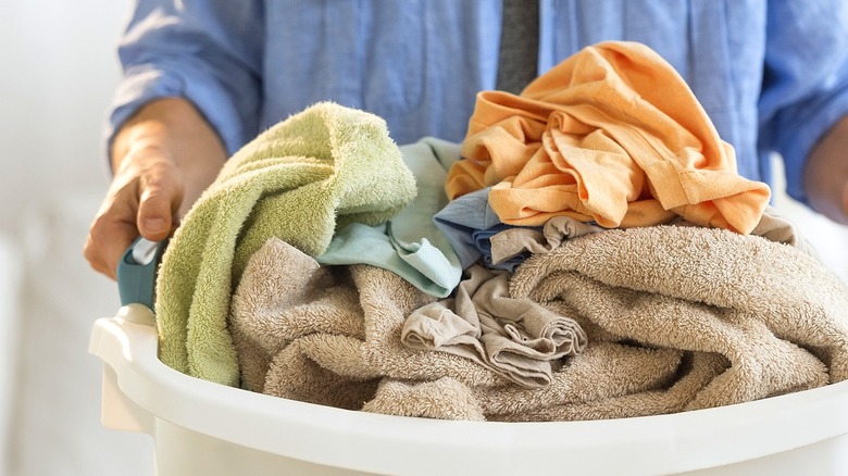 Close-up of a person wearing a blue shirt carrying a laundry basket of towels and clothes