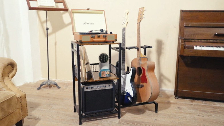 A vinyl record stand with a built-in guitar rack next to a piano.
