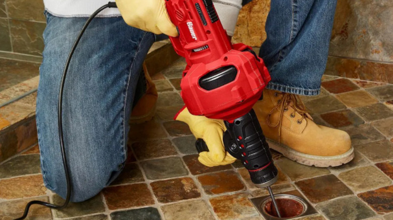 a man uses an automatic drain snake to unclog a drain