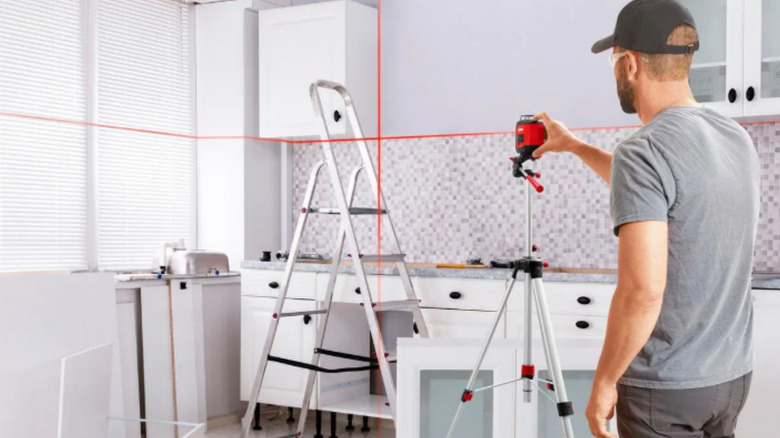 a man uses a bauer laser level to determine level cabinet placement