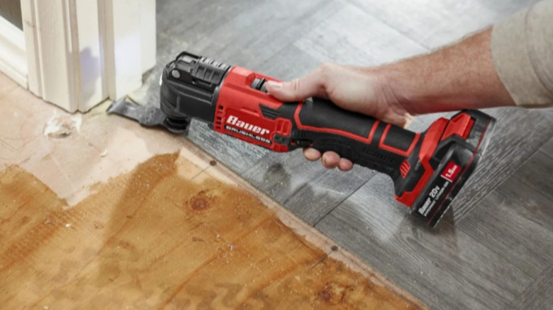 a person uses an oscillating tool to cut trim in a doorway