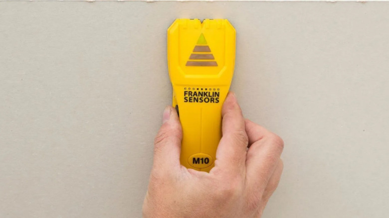 a person uses a stud finder on a sheetrock wall