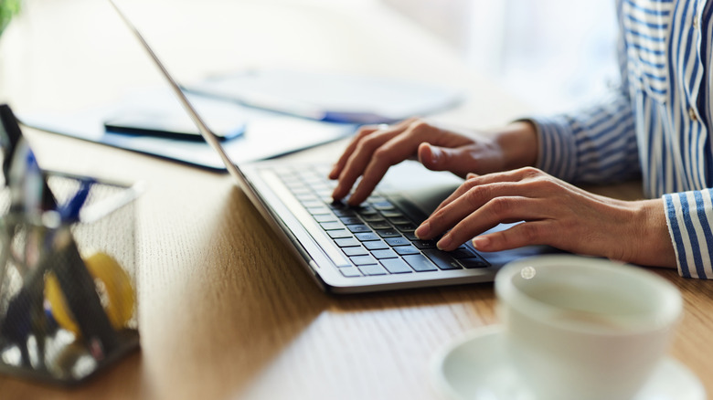 A person wearing a blue and white striped shirt uses a laptop computer