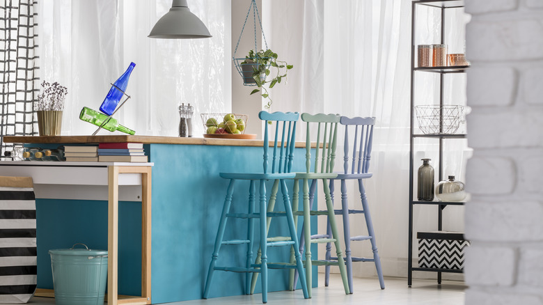 A bright blue kitchen island with three colorful chairs and bits of black and white patterns around