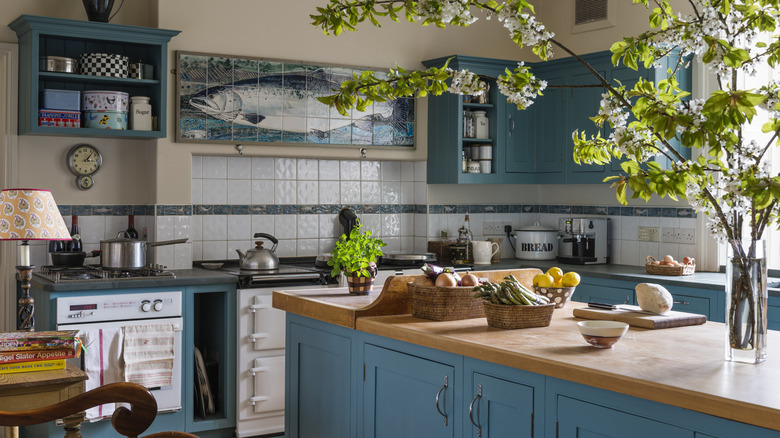 A kitchen with an island, blue-green cabinets, and a tile with a fish on it