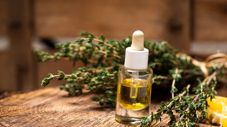 Dried thyme next to a bottle of thyme oil on a wooden tabletop
