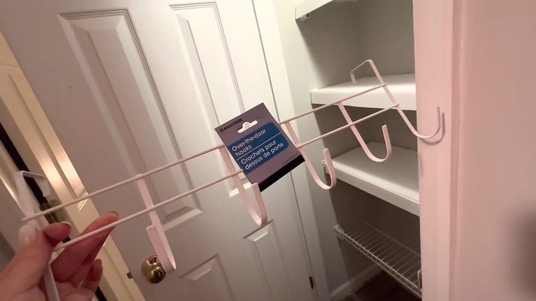 A woman's hand holds a white over the door hook set for organizing a bathroom.