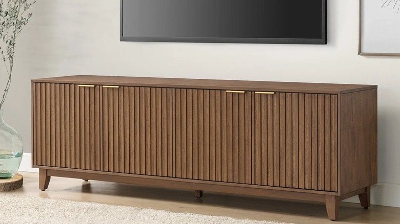A walnut brown console in a living room against a cream wall with a TV screen above it