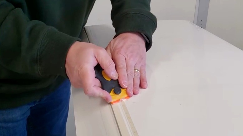 Person removing a line of adhesive with plastic razor blade