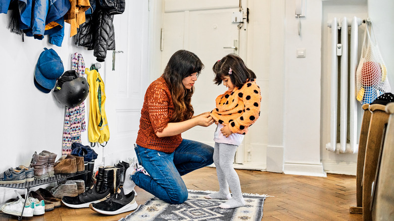 Mother zips child's jacket in mudroom 