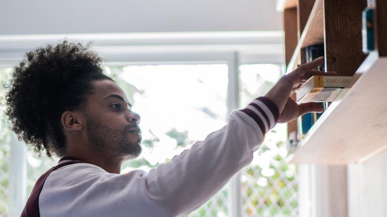 man reaching for a book on a hanging shelf