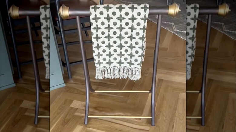 A modernized brass blanket rack holding a small throw