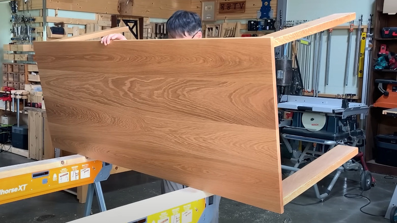 Man lifting finished white oak dining table in workroom