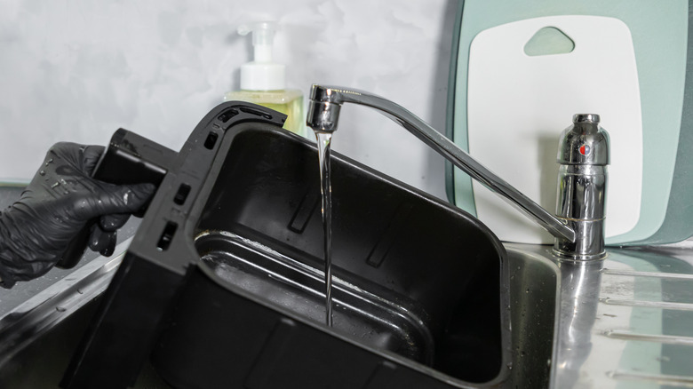 Person wearing black gloves fills an air fryer basket with water from the sink