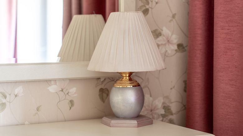 Table lamp with white fluted lampshade against floral wallpaper