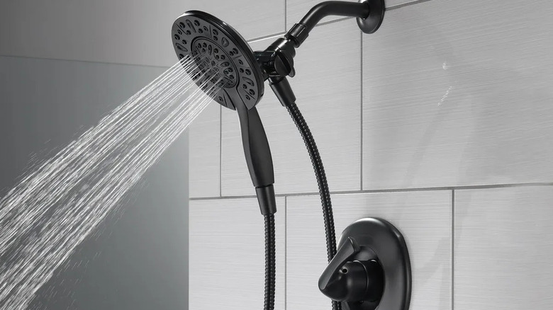 A hand holds out the hand shower away from the Delta Larkin In2ition Shower Head, both flowing with water