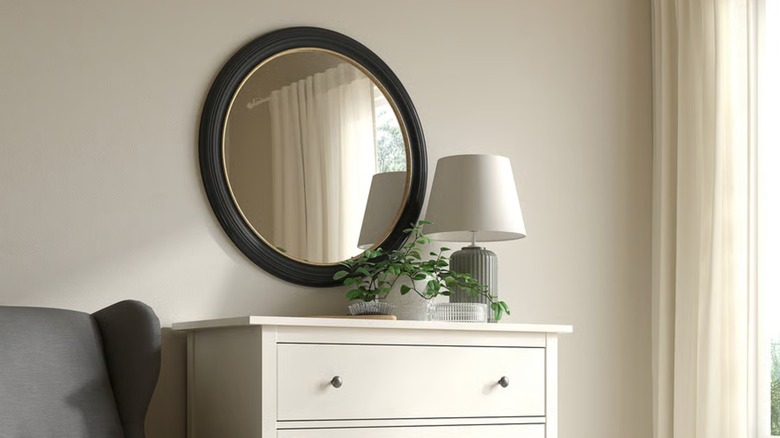 A large mirror in a traditional black frame hangs over a cream colored dresser