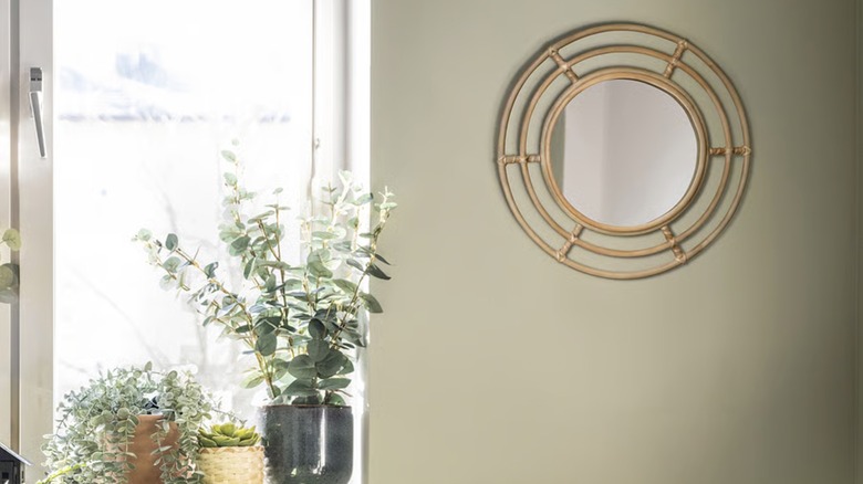 A geometric rattan mirror hangs on a wall next to a large window