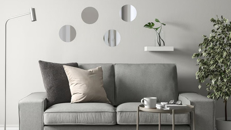 Four small mirrors are arranged on a wall above a gray sofa