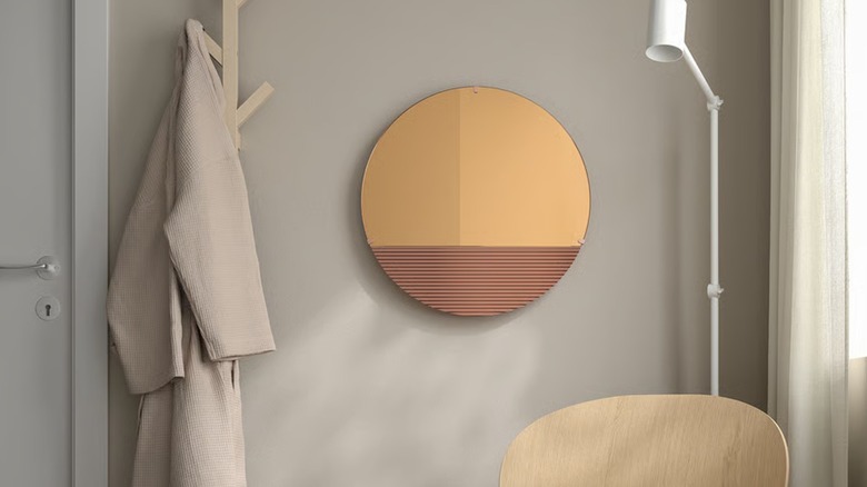 A wavy rose gold mirror from IKEA hangs on a wall next to a neutral bathrobe