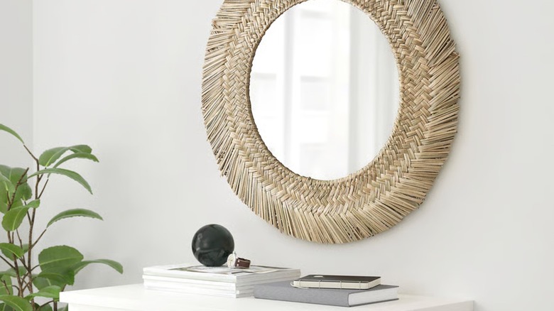 A bohemian handwoven grass framed mirror hangs over a pile of books