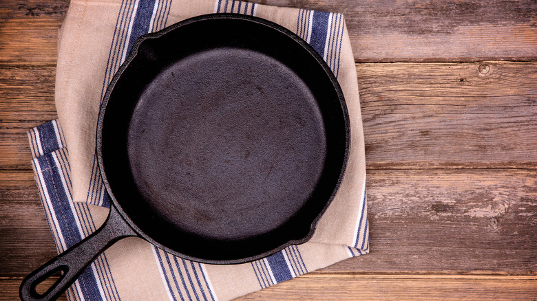A cast iron skillet sits on a striped tea towel on a wood table
