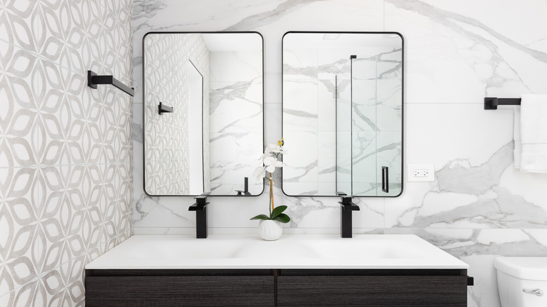 A bathroom with white marble walls and black accents on cabinets, mirrors, and hardware