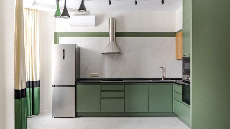 A white kitchen with green cabinets, green and black light fixtures, and a white curtain with green and black color block on the bottom