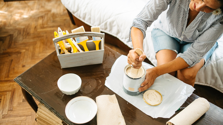 A person mixing a sandy paint color on a coffee table with paintbrushes and bowls nearby