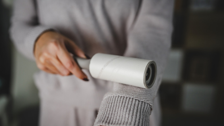 A woman's hand using a lint roller to clean sweater sleeve