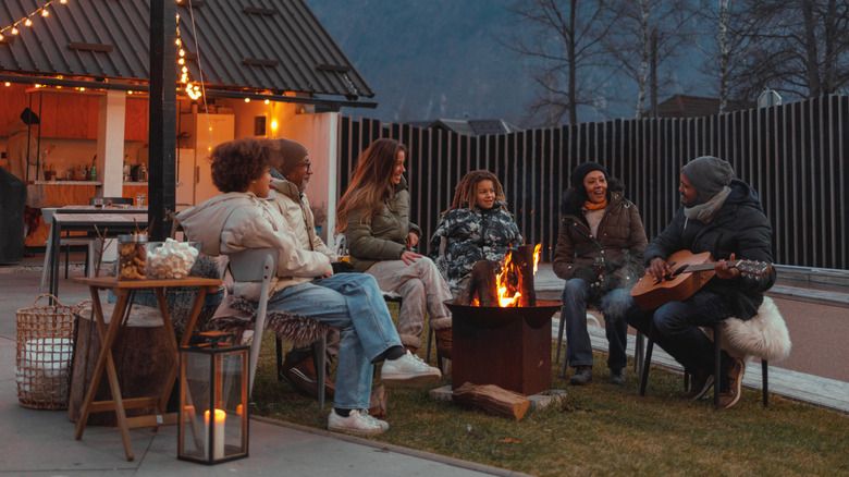 Group of friends hanging around fire pit in backyard