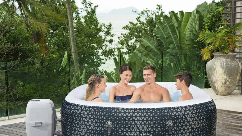 A family enjoys a Saluspa inflatable jacuzzi on a patio surrounded by tropical plants