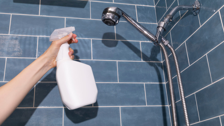 Person spraying shower head with cleaning solution