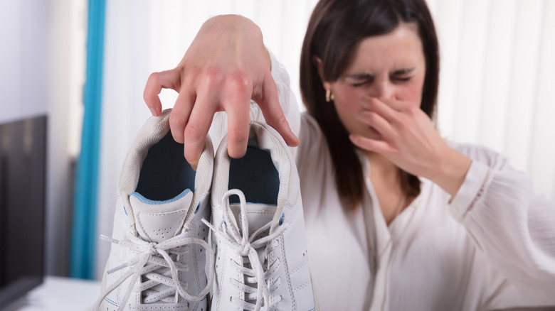woman holding stinky shoes while plugging nose