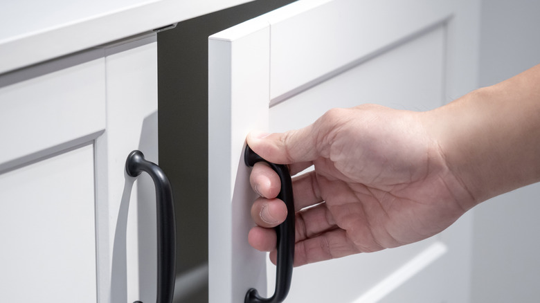 A hand closing a white cabinet door with a black handle