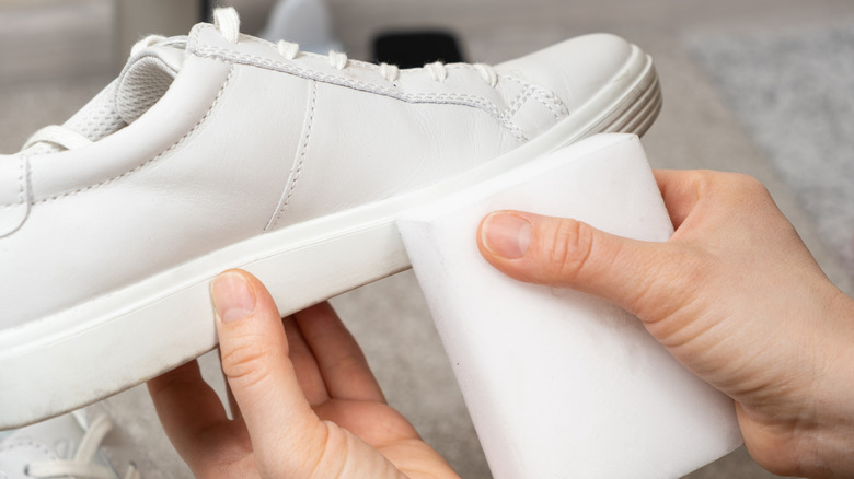 A person cleans a white sneaker with a melamine sponge.