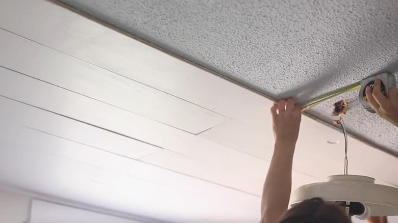 Person measuring ceiling while installing plywood planks
