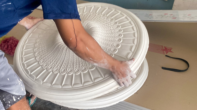 A person handles a large white ceiling medallion