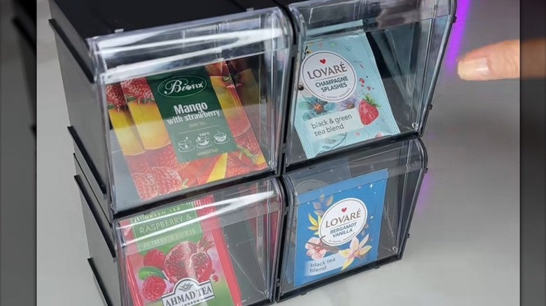 Black stacking containers holding assortment of tea bags, including mango with strawberry, black and green, and bergamot vanilla
