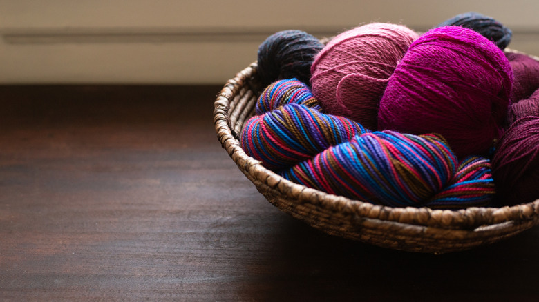 A bowl of colorful spools of yarn in purple, blue, rainbow, and pink colors.