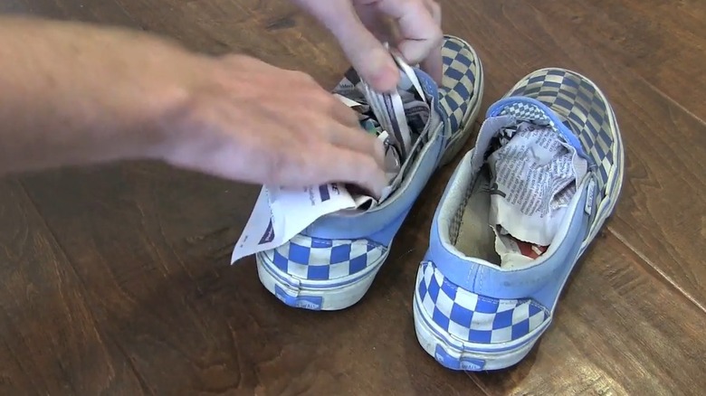 Hand stuffing balled up newspapers in a blue and white fabric shoe