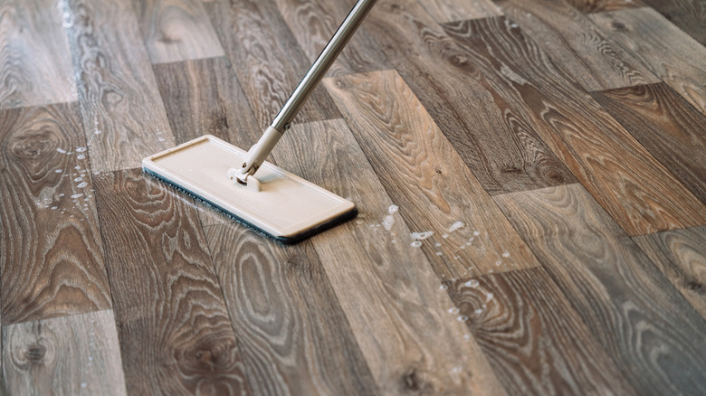 A mop on a faux wood laminate floor with water and soap bubbles.