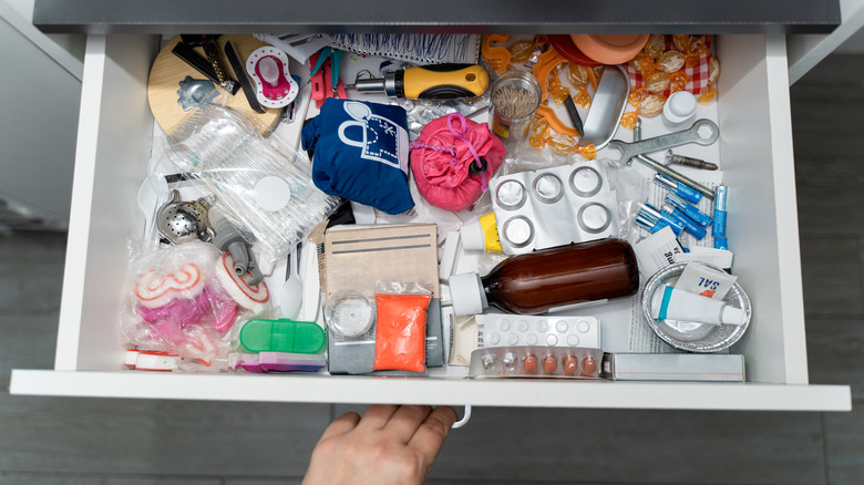 A hand opening a cluttered drawer, packed with random items