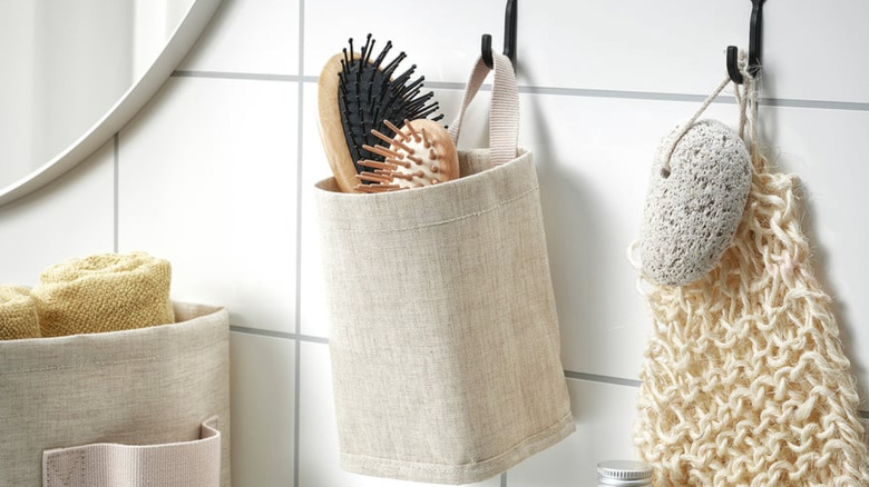 IKEA PURRPINGLA filled with brushes hanging on a hook on a bathroom wall.